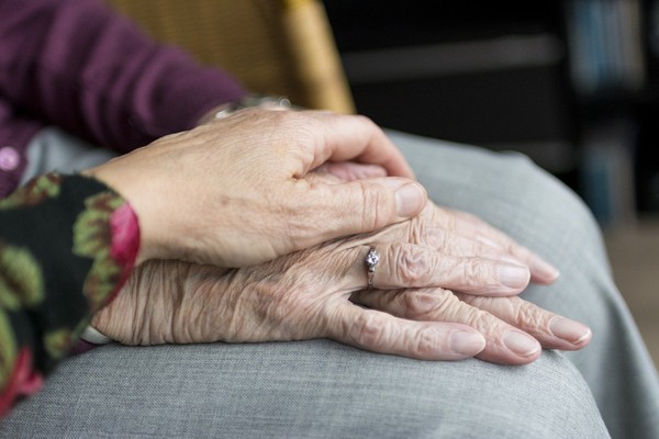 Eine pflegende Hand hält die Han einer älteren Person.